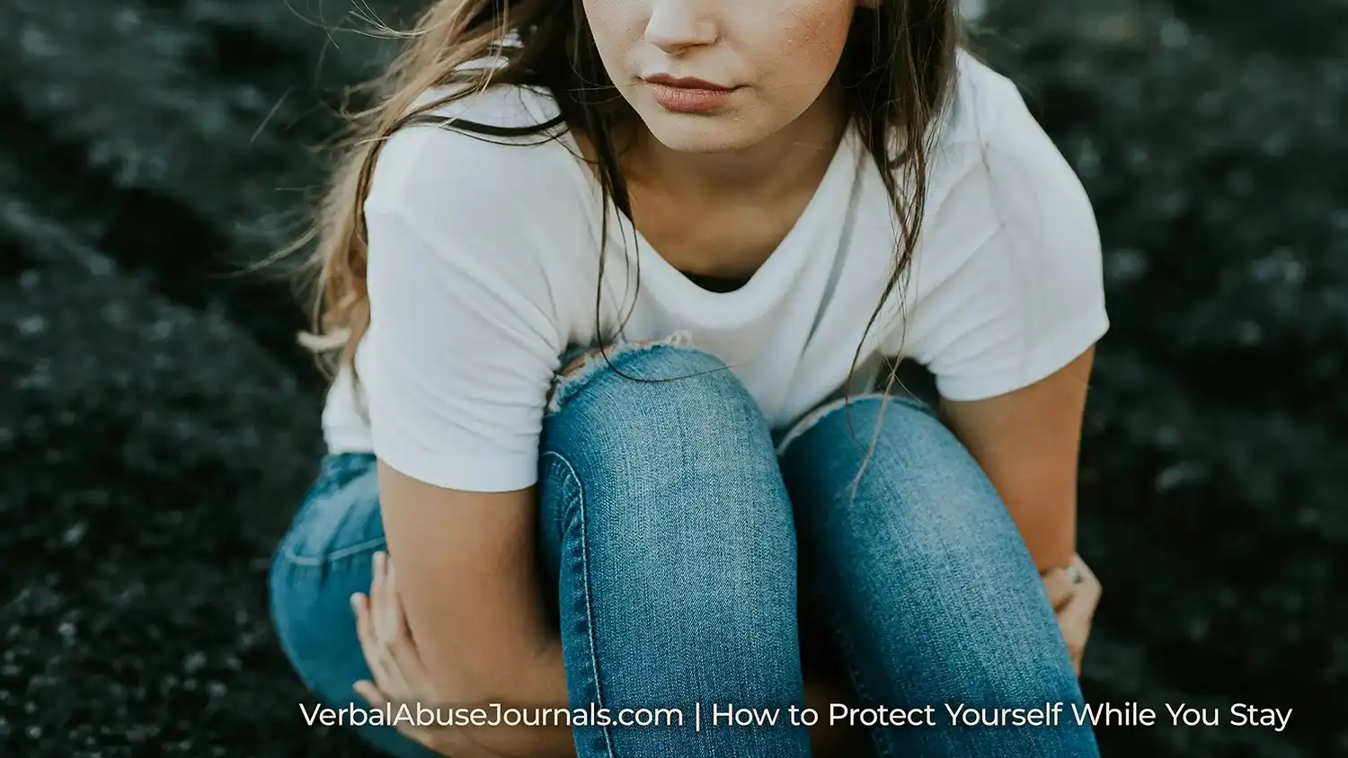 Woman sitting on ground with arms wrapped around her legs